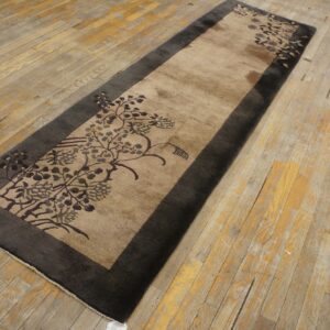 Tan and charcoal runner rug with floral pattern, lying on worn wood plank flooring.