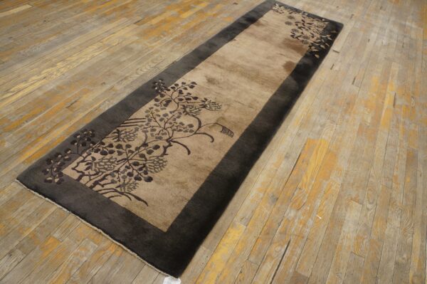 Tan and charcoal runner rug with floral pattern, lying on worn wood plank flooring.