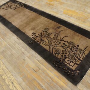 Tan and charcoal runner rug with a bold, dark floral motif lying on patchy wood planks.
