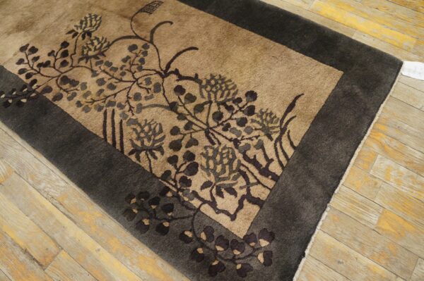 A brown and tan floral rug with a dark border lies on distressed light wood flooring.
