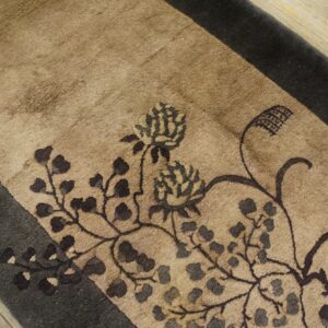 The beige rug displays a stylized dark floral pattern and wide border on rustic wood planks.