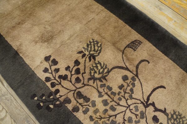 The beige rug displays a stylized dark floral pattern and wide border on rustic wood planks.
