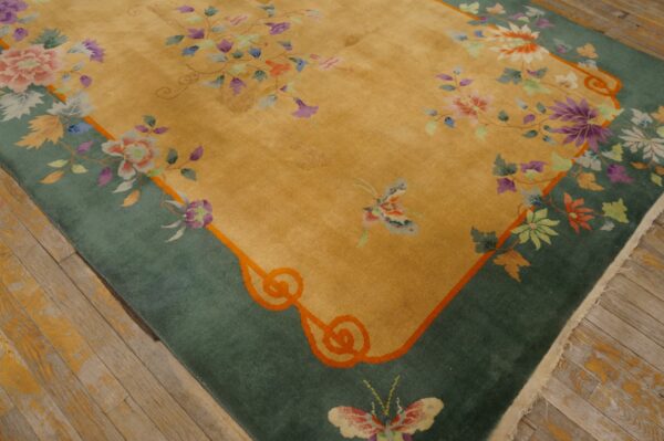 A golden rug featuring a wide teal border and colorful floral and butterfly motifs rests on a wood floor.