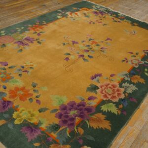 Saffron yellow rug with a green border and multicolored floral designs sits on natural wood plank flooring.