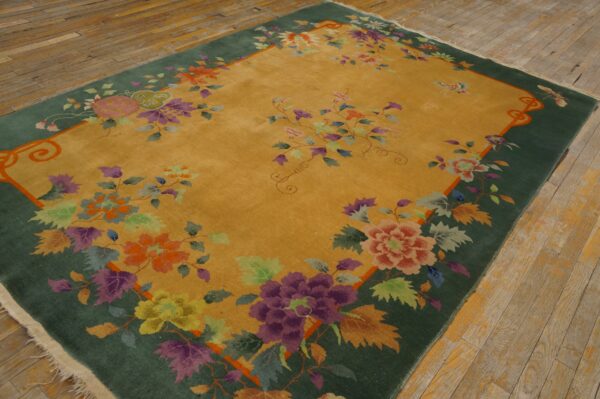 Saffron yellow rug with a green border and multicolored floral designs sits on natural wood plank flooring.
