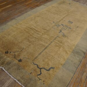 A gold and sage rug featuring an abstract dark blue pattern rests on distressed wooden floorboards.