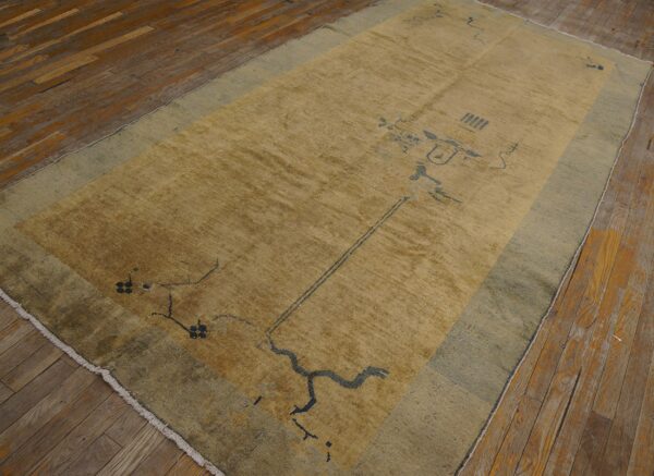 A gold and sage rug featuring an abstract dark blue pattern rests on distressed wooden floorboards.