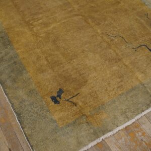 Distressed gold and olive green rug featuring minimal dark floral designs on worn wood flooring.