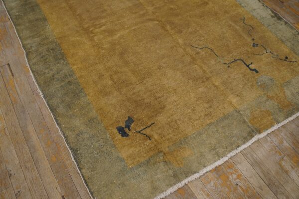 Distressed gold and olive green rug featuring minimal dark floral designs on worn wood flooring.