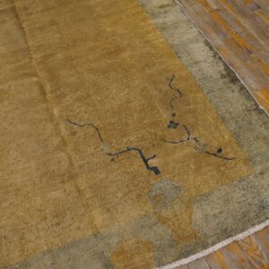 Low pile gold rug with sparse black designs and a distressed olive border on worn wood flooring.