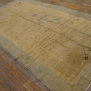 Low-pile gold rug with dark abstract motifs and a wide sage border on hardwood floors.