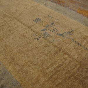 A faded gold rug with sparse gray geometric motifs and a pale blue border rests on wood planks.