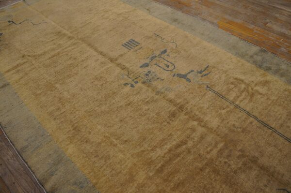 A faded gold rug with sparse gray geometric motifs and a pale blue border rests on wood planks.