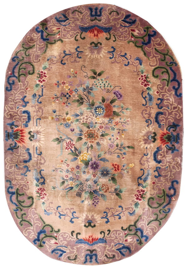 Tan oval rug featuring a dense multicolored floral bouquet and a wide mauve border with blue accents.