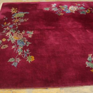 A deep crimson rug with medium pile and scattered colorful floral designs rests on light wood plank flooring.