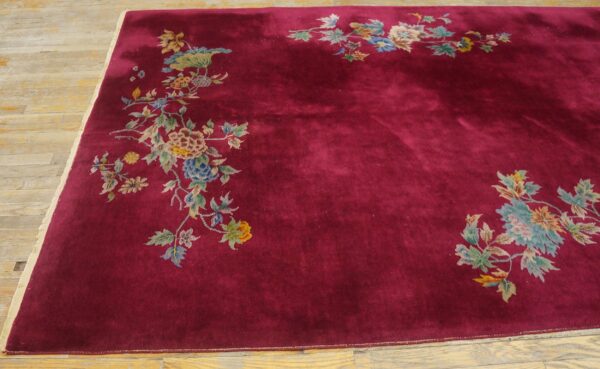 A deep crimson rug with medium pile and scattered colorful floral designs rests on light wood plank flooring.