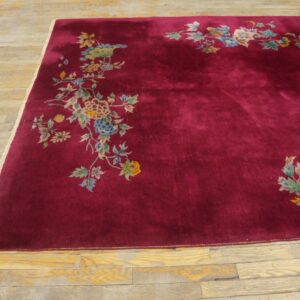 Maroon rug with colorful floral corner designs rests on distressed wood planks.