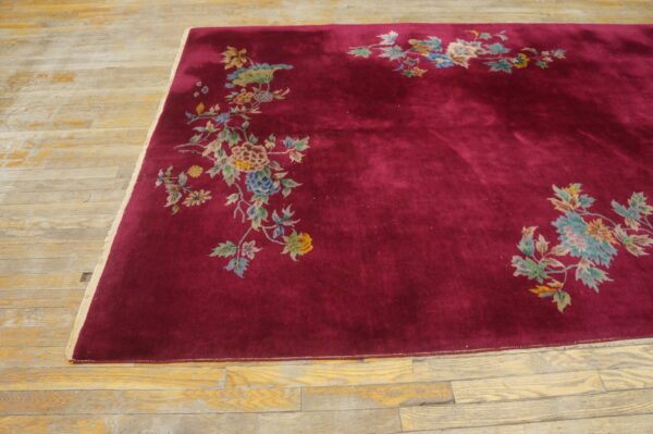 Maroon rug with colorful floral corner designs rests on distressed wood planks.