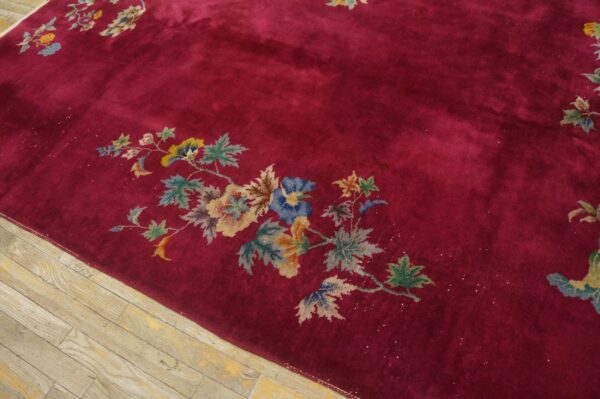 A plush crimson rug with multicolor scattered floral motifs lies partially over rustic light wood flooring.