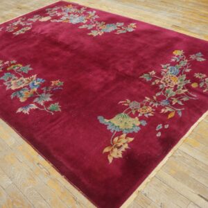 A deep magenta velvety rug features pastel floral clusters along the perimeter on light, worn wood flooring.