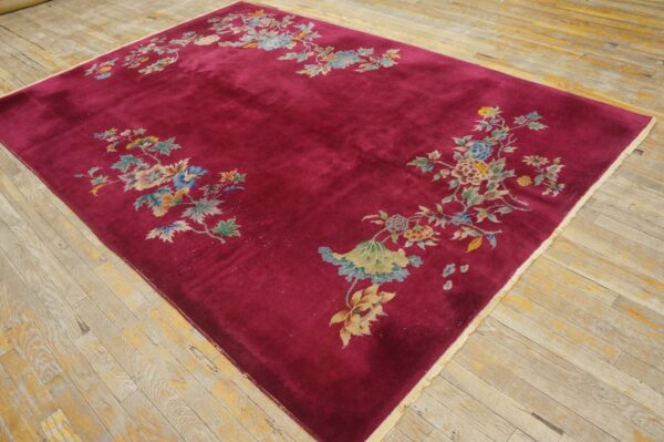 A deep magenta velvety rug features pastel floral clusters along the perimeter on light, worn wood flooring.