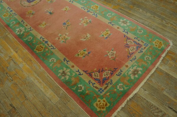 Low-pile pink rug with scattered multicolored flowers and a wide green border on distressed wood.