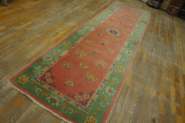 Pink floral runner with green borders and a central medallion rests on worn hardwood planks.