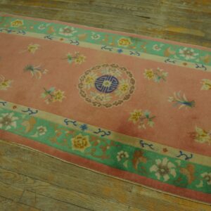 Pink runner rug with a floral pattern and central medallion, bordered in teal and beige, on wood planks.