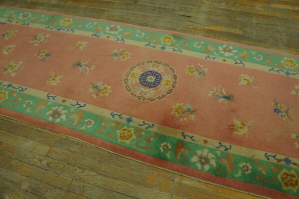 Pink runner rug with a floral pattern and central medallion, bordered in teal and beige, on wood planks.