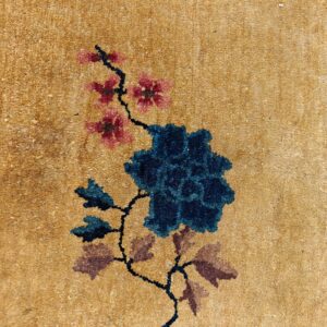 Textured tan rug detail with a prominent dark blue flower and branching pink blossoms.