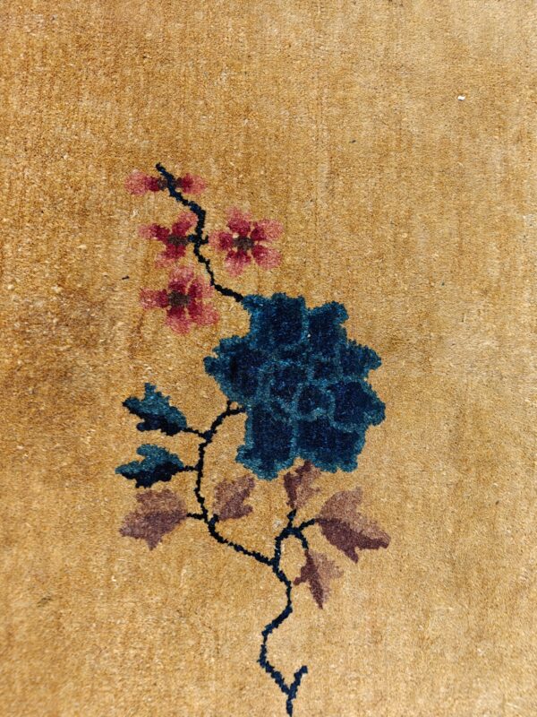 Textured tan rug detail with a prominent dark blue flower and branching pink blossoms.