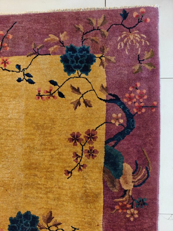 Gold and plum rug border with teal, pink, and tan flowering branch motifs on white tile.