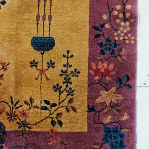 Close-up of a golden yellow rug field with a purple border patterned with teal, rust, and pink florals.