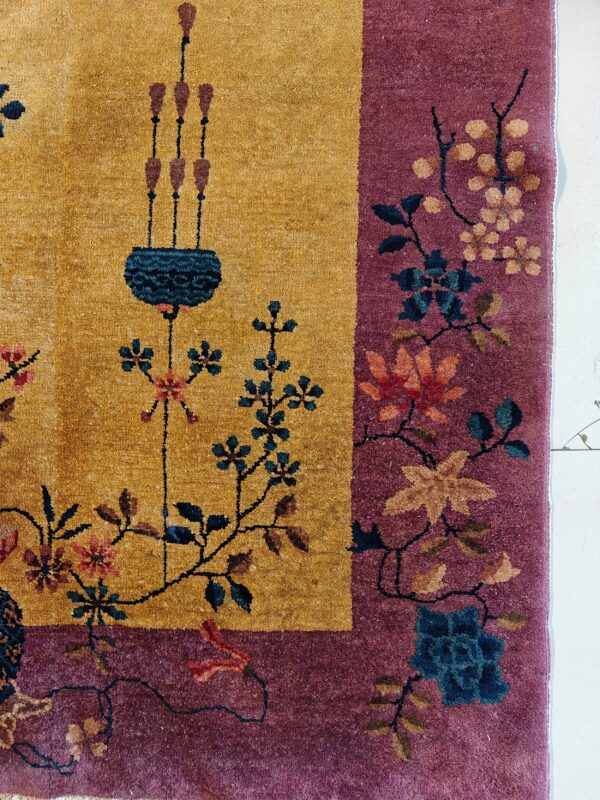 Close-up of a golden yellow rug field with a purple border patterned with teal, rust, and pink florals.