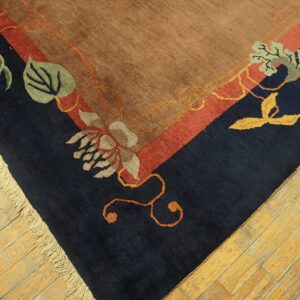 Tan rug corner with navy and red border bands, detailed floral patterns, and light fringe on wood floors.