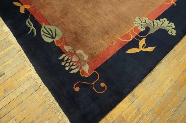 Tan rug corner with navy and red border bands, detailed floral patterns, and light fringe on wood floors.