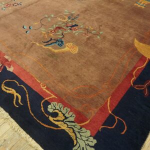 A tan and multicolored floral rug with a wide navy and red border sits on wood flooring.