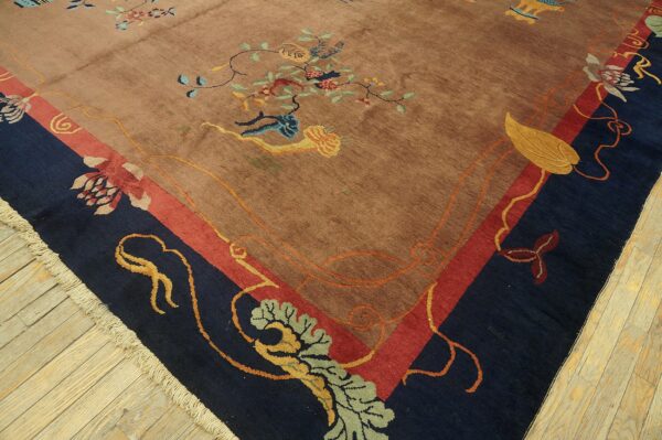 A tan and multicolored floral rug with a wide navy and red border sits on wood flooring.