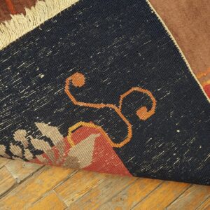 The dark, speckled woven backing of a brown and red patterned rug lays on distressed wood floors.
