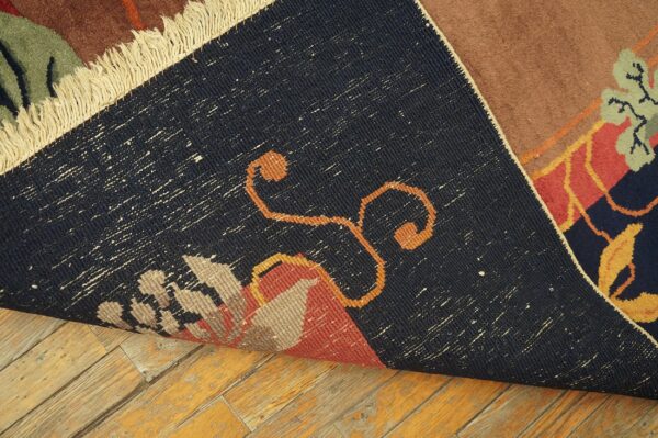 The dark, speckled woven backing of a brown and red patterned rug lays on distressed wood floors.