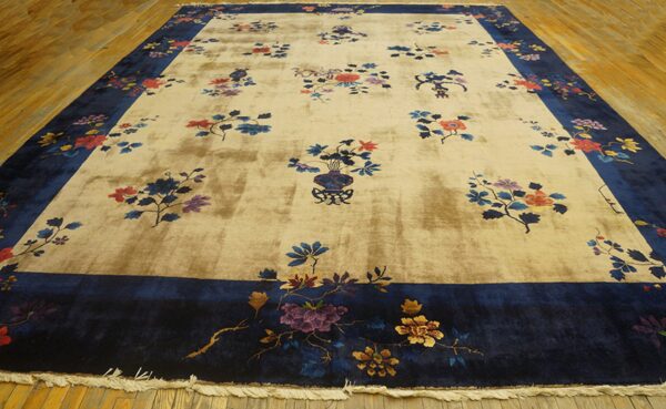 Beige rug with a high sheen, navy blue border, and scattered colorful floral designs on wood flooring.