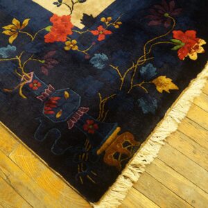 High-pile navy rug with red, gold, and blue florals and a vase motif on rustic wood flooring.