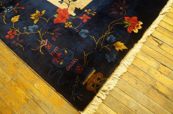 High-pile navy rug with red, gold, and blue florals and a vase motif on rustic wood flooring.