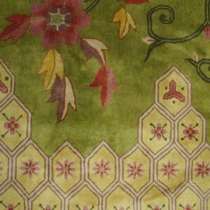 Plush olive green rug with red floral vines and a complex geometric border of interlocking yellow hexagons.