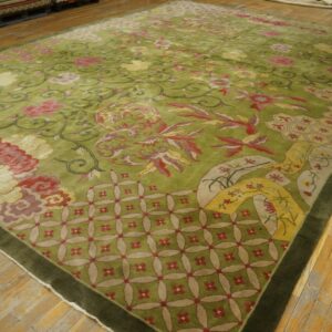 Plush olive green rug with intricate pink, red, and cream floral designs covers a light wood floor.