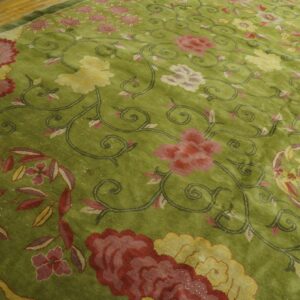 Textured green rug with red, pink, and yellow floral designs resting on light wood flooring.