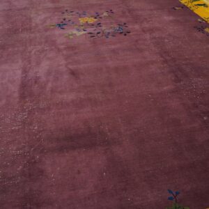 Distressed plum rug with a centered floral motif and a wide yellow patterned border on wood flooring.