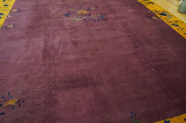 Distressed plum rug with a centered floral motif and a wide yellow patterned border on wood flooring.