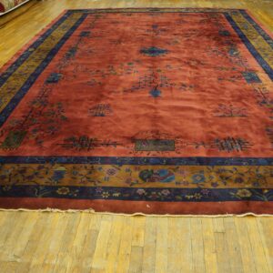 A rust rug with blue and gold ornate borders sits on yellow plank hardwood flooring.