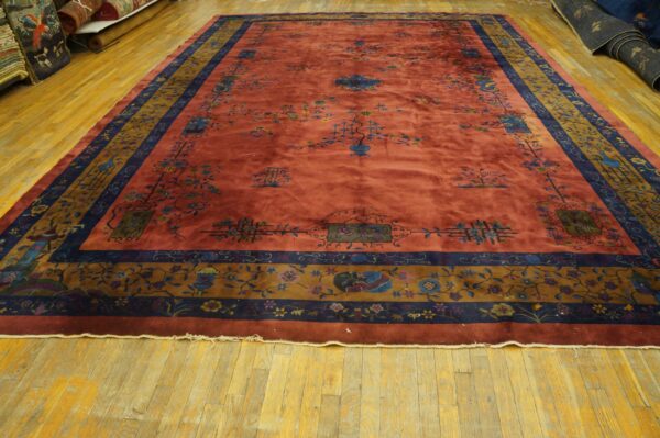 A rust rug with blue and gold ornate borders sits on yellow plank hardwood flooring.
